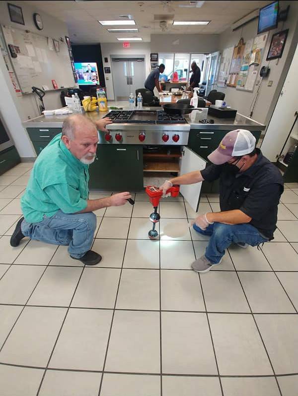 Two DrainCo technicians examining a floor drain in a commercial kitchen